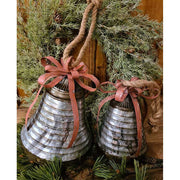 Rusztikus vidéki stílusú, óriás méretű, 25 cm magas, antikolt felületű, piros színű fém masnival díszített karácsonyi kézműves bádogharang fenyőkoszorúval antikolt fa deszkaasztalon 