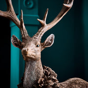 Erdei fenyőtoboz koszorúval díszített, nagyméretű karácsonyi szarvas figura.