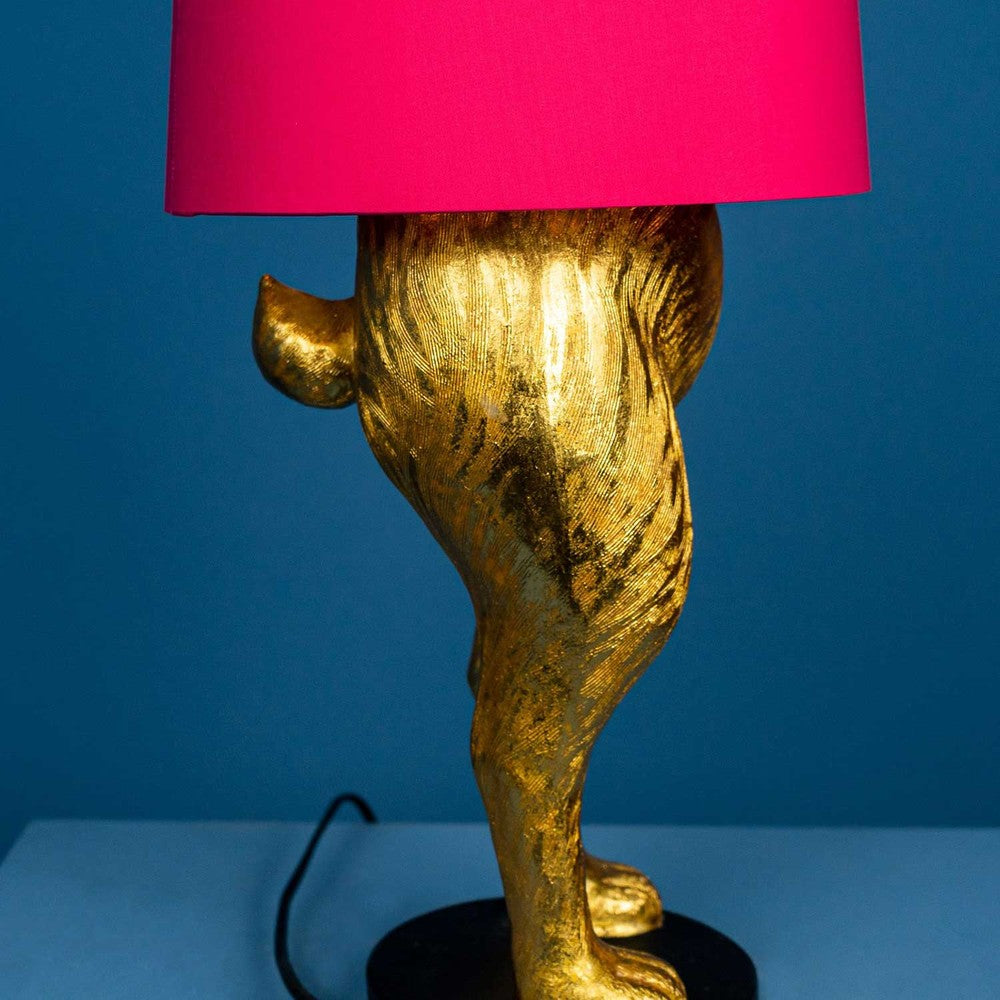 Aranyszínű, rejtőzködő nyuszi figurás, 74 cm magas, kortárs, glamour stílusú, díjnyertes dizájn asztali lámpa, pink színű lámpaernyővel, kékszínű háttér előtt.