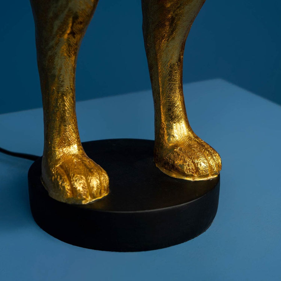 Aranyszínű, rejtőzködő nyuszi figurás, 74 cm magas, kortárs, glamour stílusú, díjnyertes dizájn asztali lámpa, pink színű lámpaernyővel, kékszínű háttér előtt.