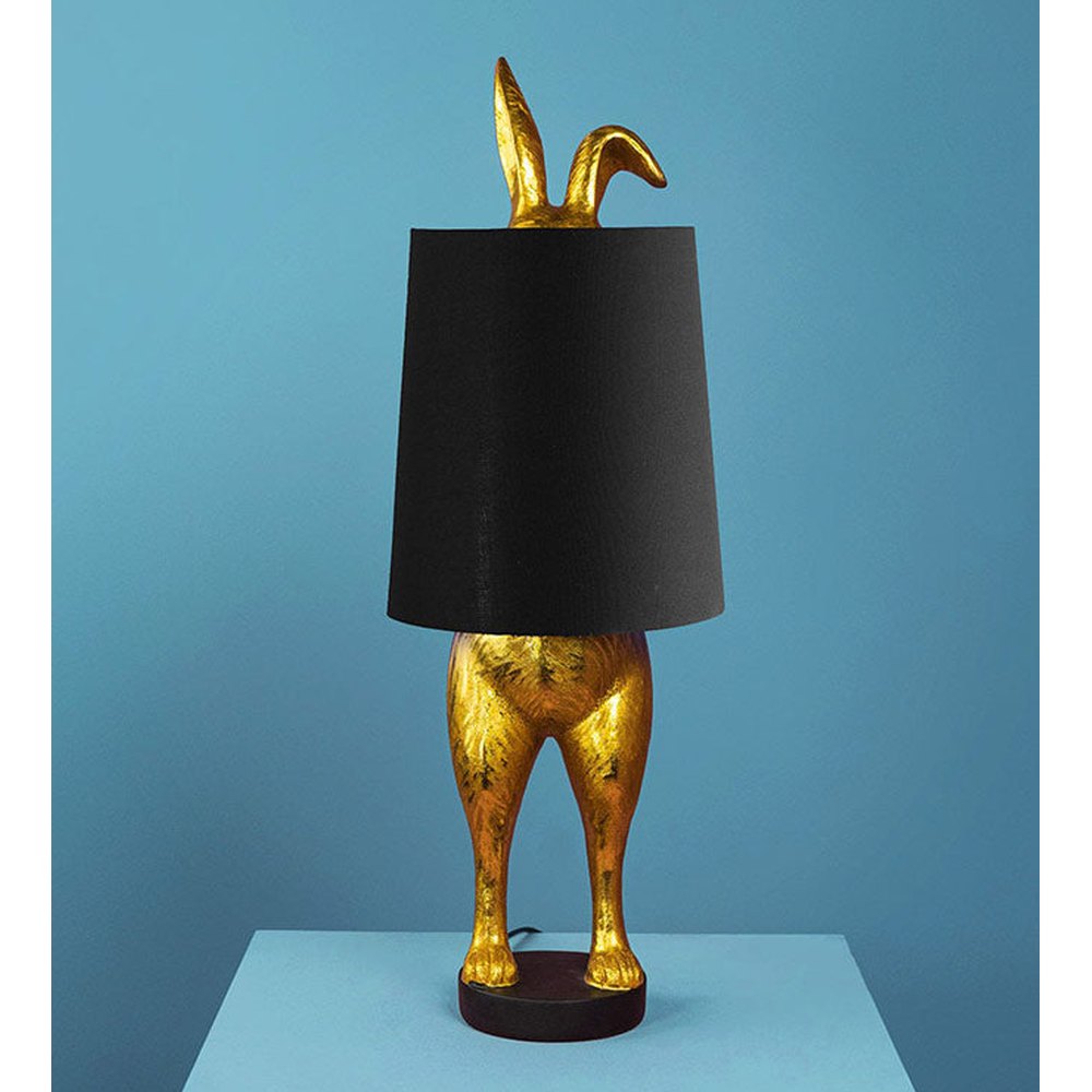 Aranyszínű, rejtőzködő nyuszi figurás, 74 cm magas, kortárs, glamour stílusú, díjnyertes dizájn asztali lámpa, feketeszínű lámpaernyővel, kék háttér előtt.