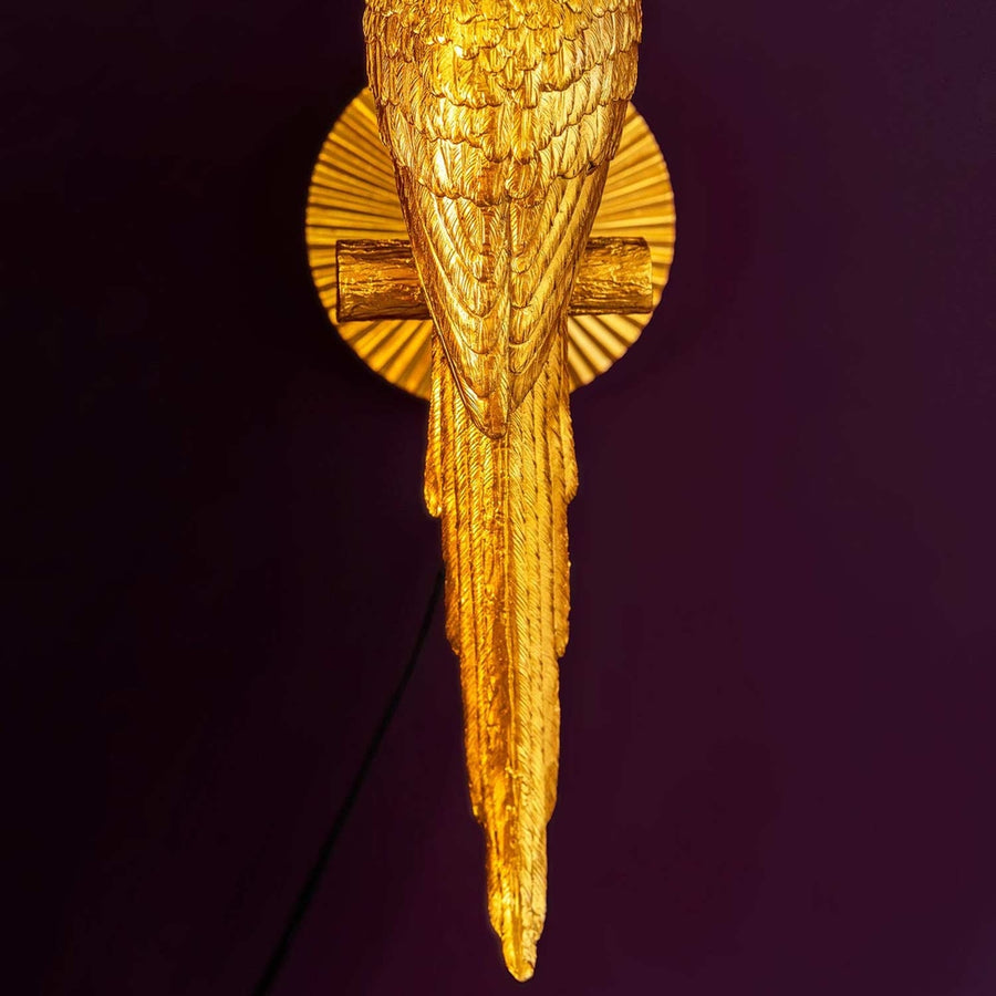 Arany színű papagáj hosszú farka, lila színű háttér előtt. 