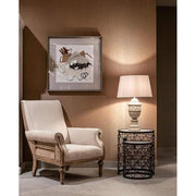 Prémium kategóriás, gyarmati stílusú, újrahasznosított trópusi fából készült, ekrü színű szövettel kárpitozott fotel barna fal előtt szürke padlón, koloniál asztali lámpával dohányzóasztalon