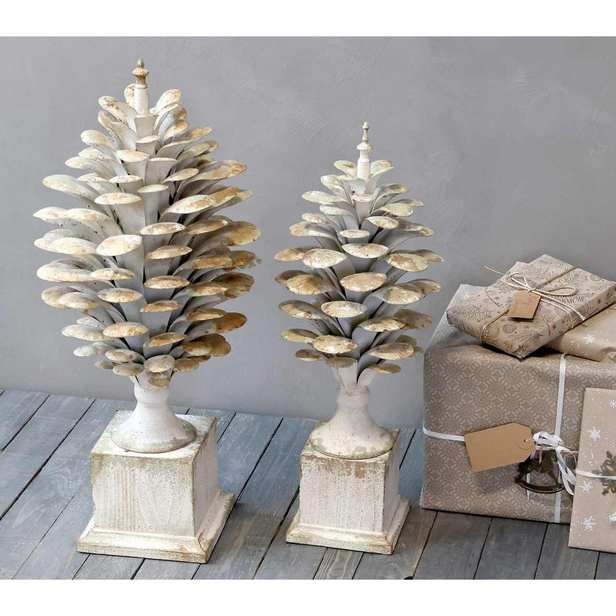 Kétféle méretű, antikolt krémszínű, fém toboz dísz szürke fal előtt, karácsonyi ajándékokkal.