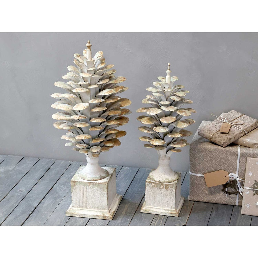Kétféle méretű, antikolt krémszínű, fém toboz dísz szürke fal előtt, karácsonyi ajándékokkal.