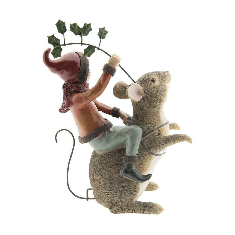 Barna színű erdei egér hátán utazó karácsonyi manó bordó ruhában és sállal, kezében magyallal oldalról fotózott képe