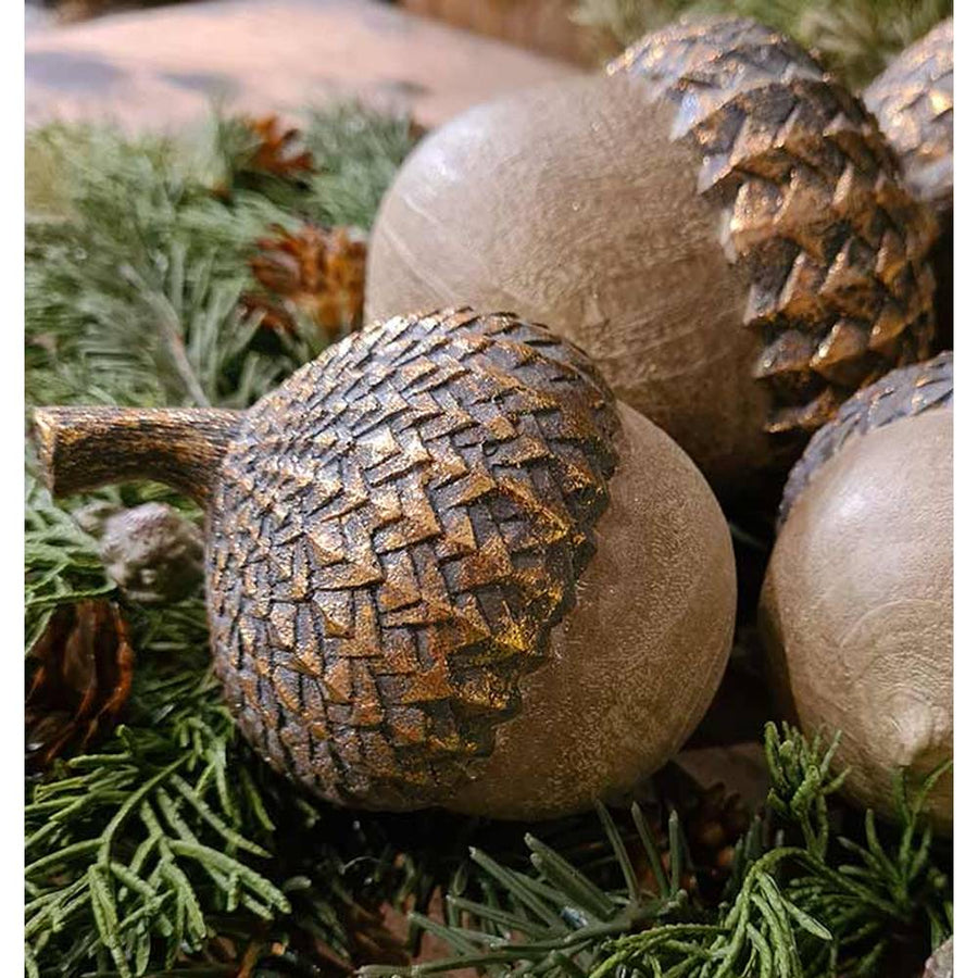 Vintage, rusztikus stílusú, 11 cm magas, fa hatású, antik arany színnel patinázott karácsonyi makk díszek fenyők között 