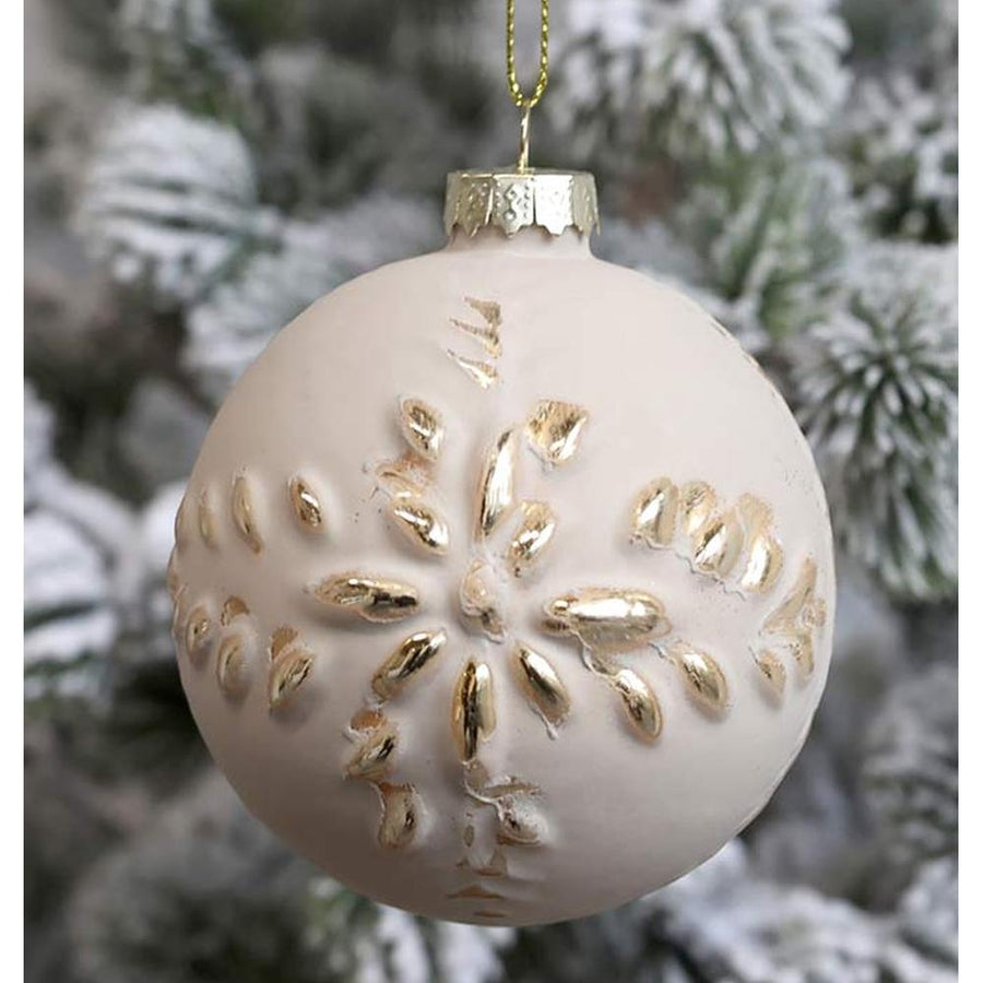 Vintage stílusú, aranyszínű növényi dombormintával díszített, gömb formájú, púderszínű üveg karácsonyfadísz, havas fenyőfán.